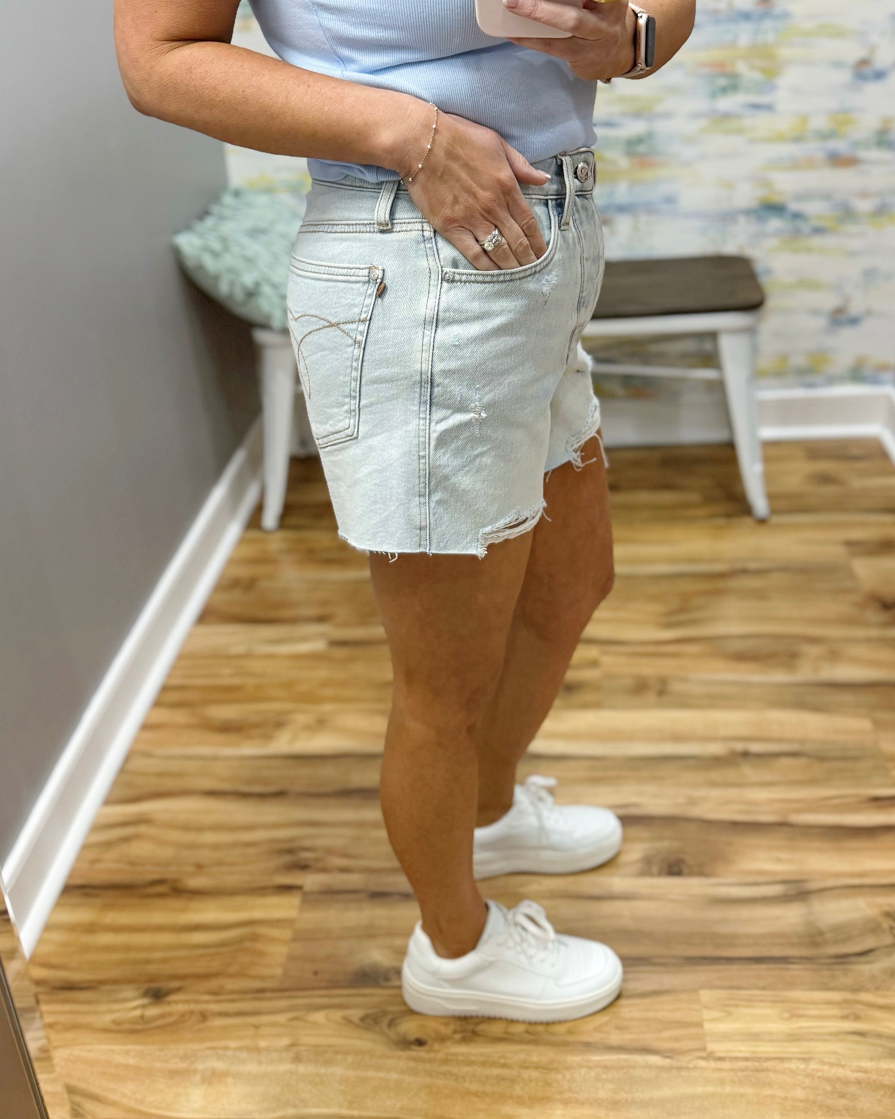 Person wearing light denim shorts and white sneakers on a wooden floor.