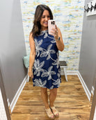 Woman taking a mirror selfie wearing a navy dress with white floral patterns in a room with a patterned wall.