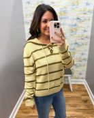 A woman taking a mirror selfie wearing a taupe and olive green striped knit hoodie sweater with drawstrings, paired with blue jeans.