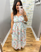 Woman taking a mirror selfie wearing a floral dress in a room with a patterned wall.