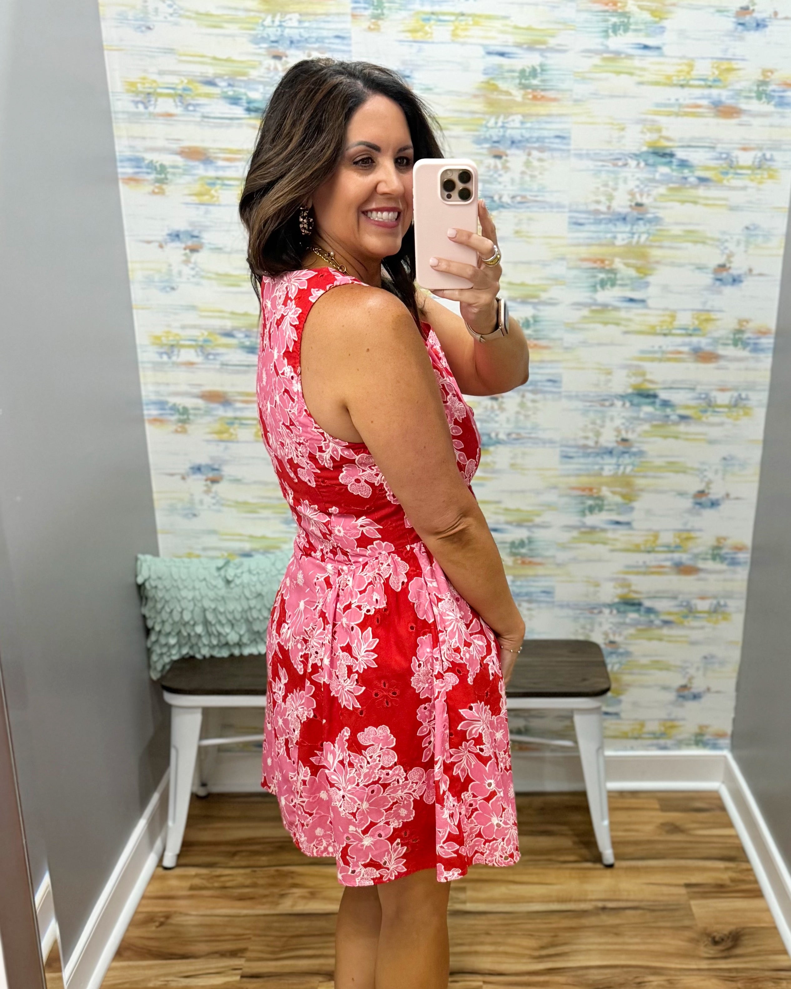 Woman taking a mirror selfie wearing a red floral dress in a room with colorful wall paper.