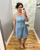 Woman taking a mirror selfie wearing a light blue denim dress in a room with a patterned wall.