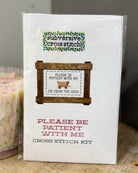 A packaged cross stitch kit labeled 'subversive cross stitch' with the design text 'PLEASE BE PATIENT WITH ME I'M FROM THE 1900s' shown on the front, photographed standing upright on a fabric surface.