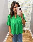 Woman taking a mirror selfie wearing a green blouse and blue jeans in a room with a colorful wall.