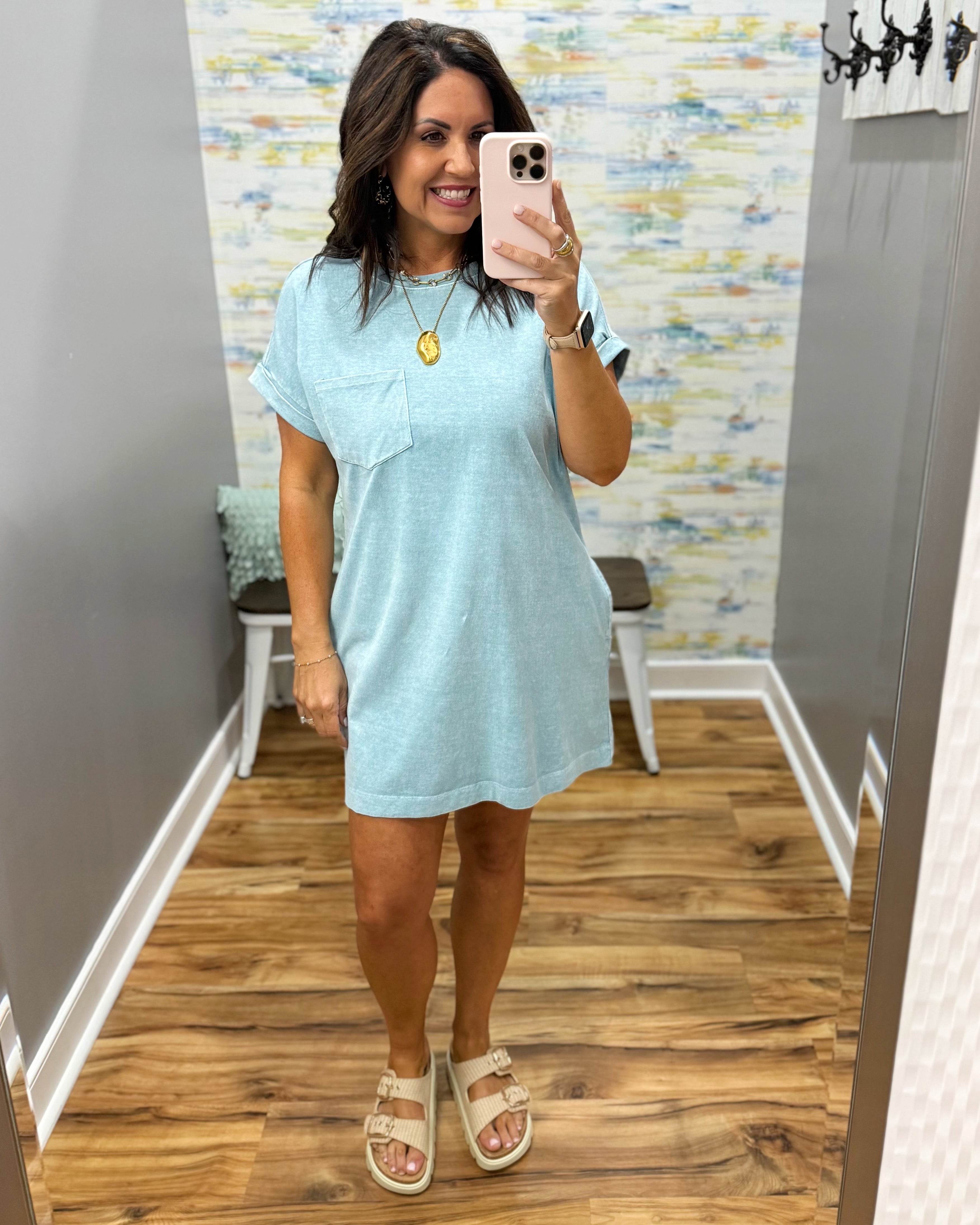 Woman taking a mirror selfie wearing a light blue dress in a room with a colorful wall.
