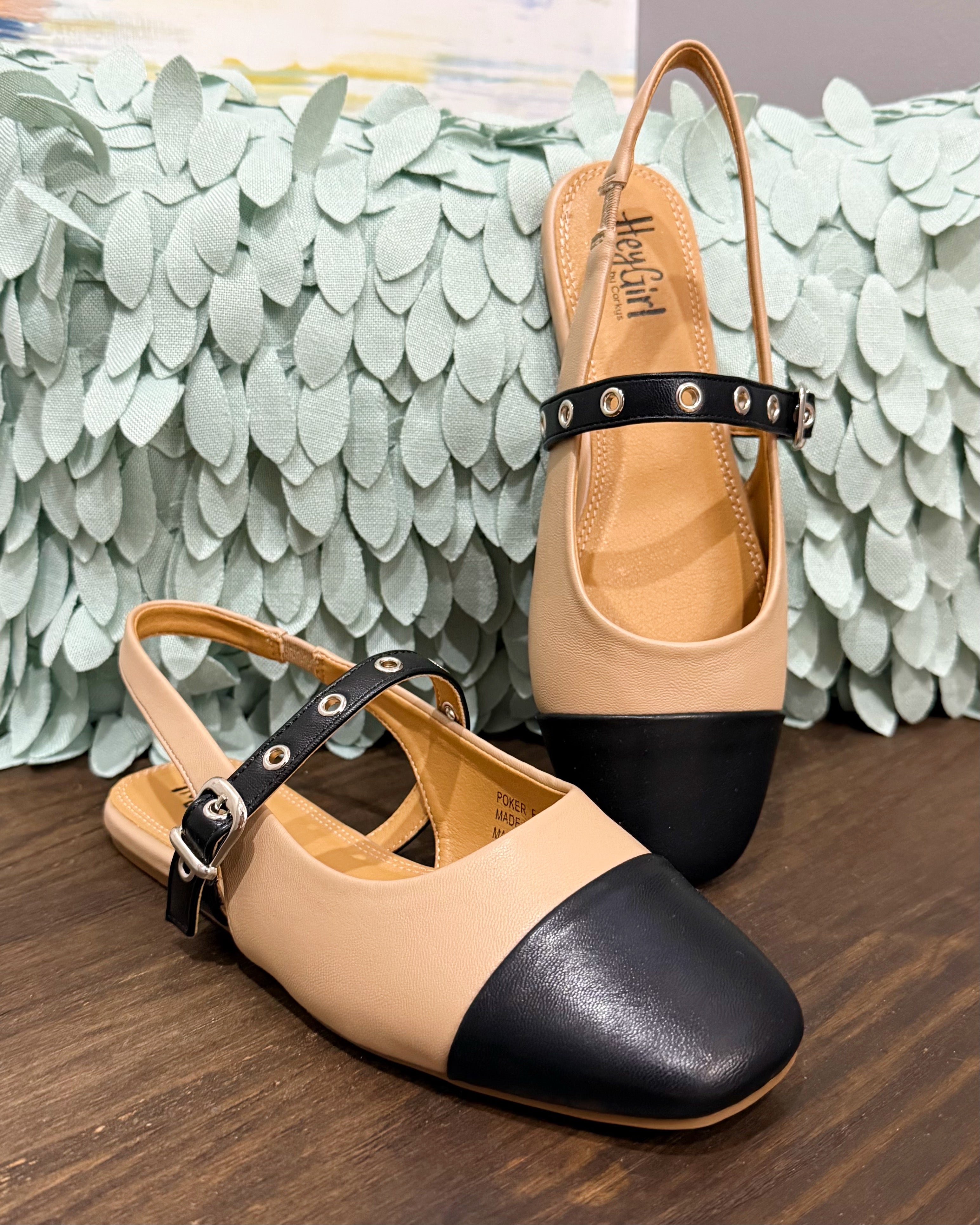 Pair of beige and black shoes on a wooden surface with a textured green wall in the background.