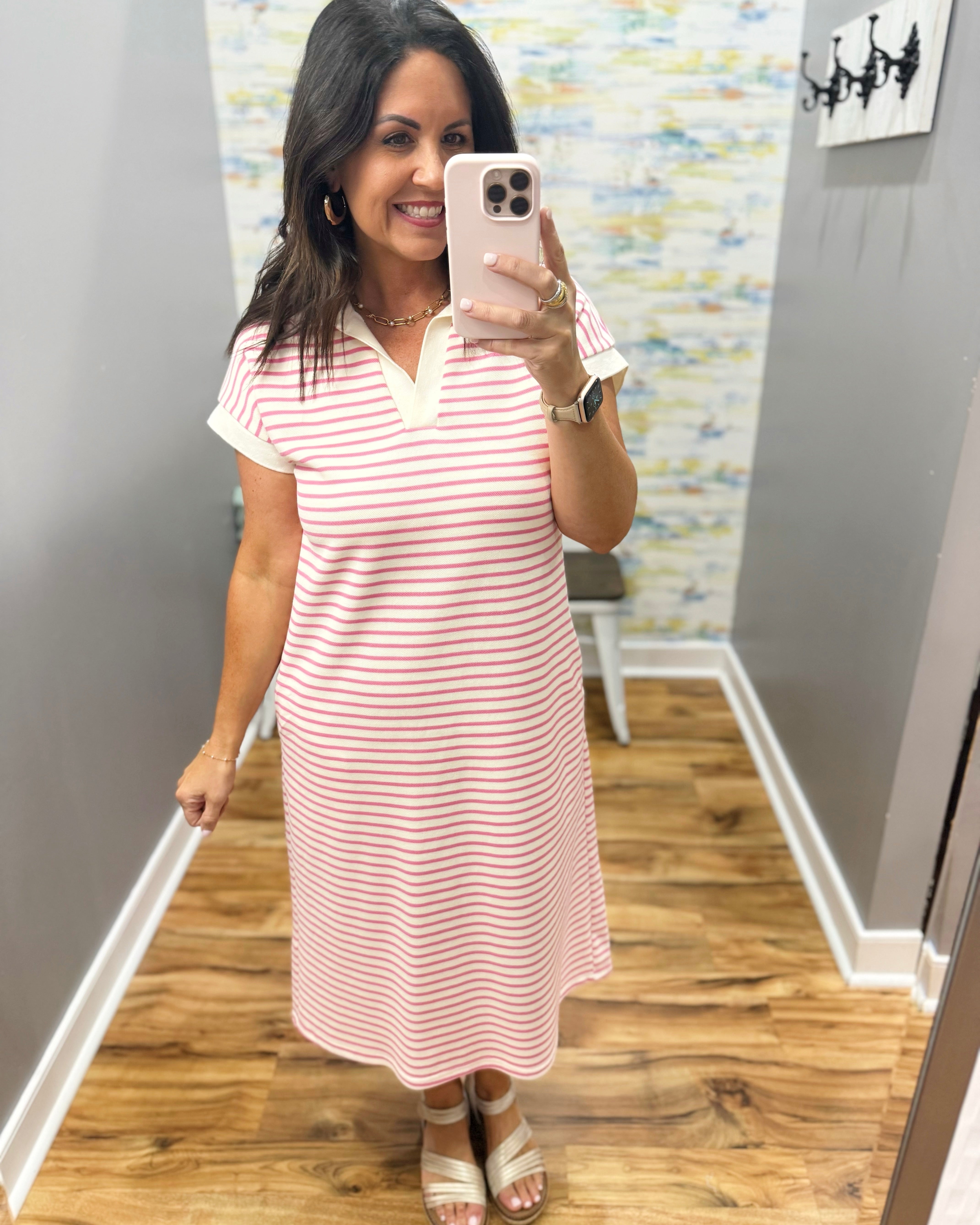 Woman taking a mirror selfie wearing a pink and white striped dress in a room with a textured wall.