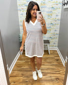 Woman taking a mirror selfie wearing a striped dress and white sneakers in a room with a colorful wall.