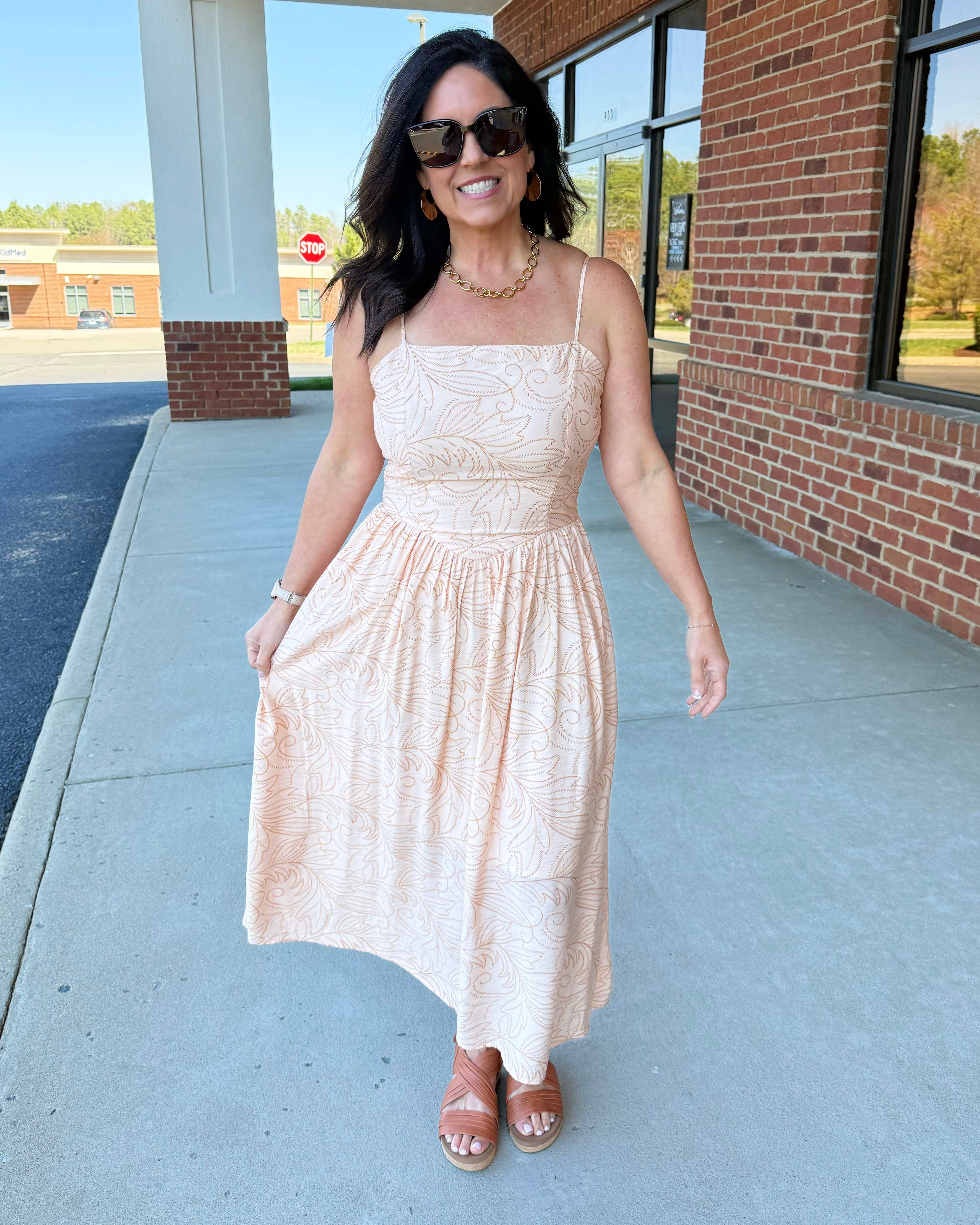 Woman in a beige dress standing on a sidewalk with a building in the background