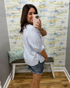 Woman taking a mirror selfie wearing a striped shirt and denim shorts in a room with colorful wall paper.