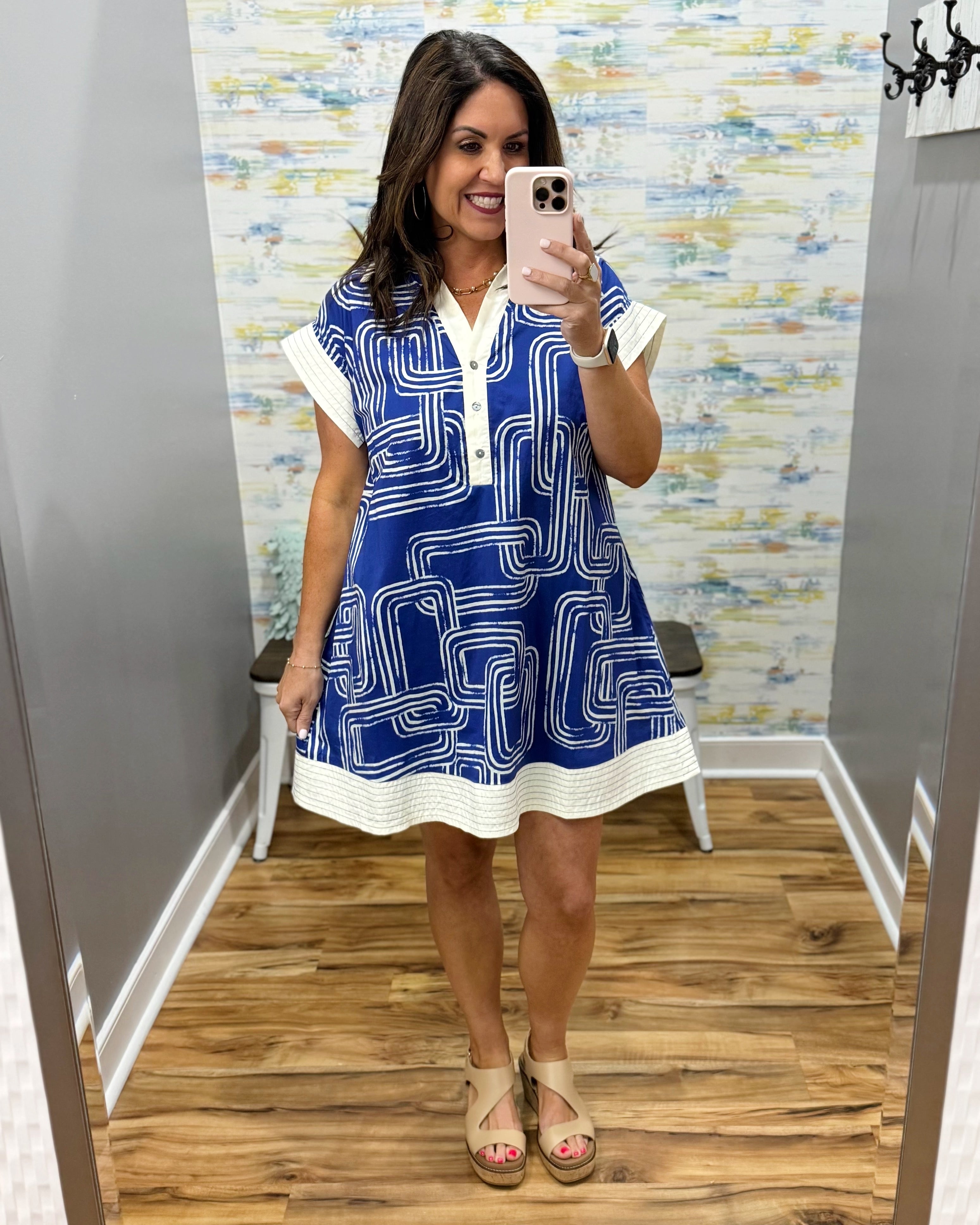 Woman taking a mirror selfie wearing a blue and white dress with a pattern.