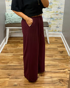 A woman takes a mirror selfie in a fitting room wearing a black short-sleeve sweater and high-waisted wide-leg pants in merlot with Corkys Sober Up shoes in leopard.