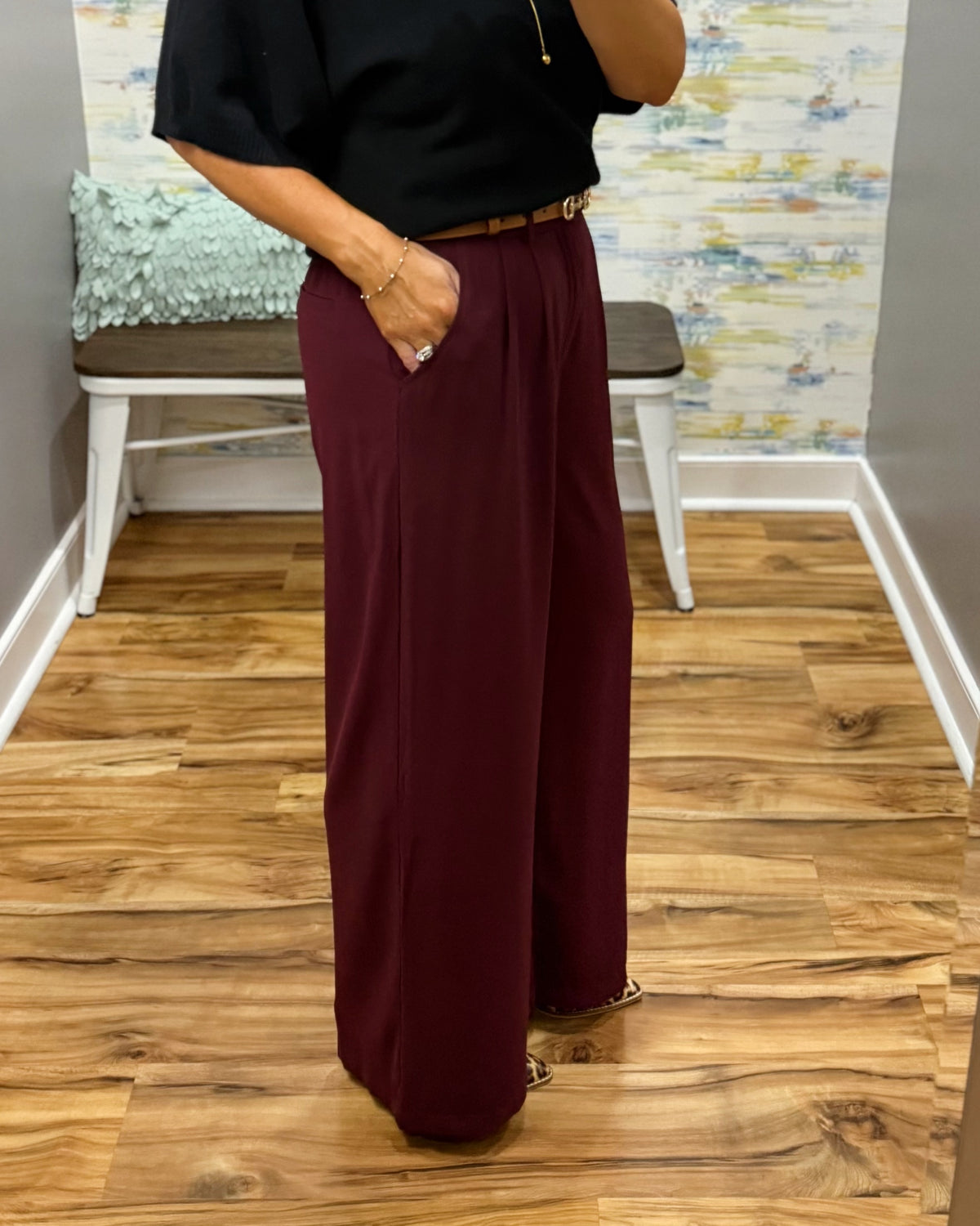A woman takes a mirror selfie in a fitting room wearing a black short-sleeve sweater and high-waisted wide-leg pants in merlot with Corkys Sober Up shoes in leopard.