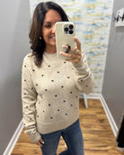 A woman takes a mirror selfie wearing a cream-colored knit sweater with small black polka dots and blue jeans in a home setting.