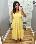 Woman wearing a yellow dress taking a mirror selfie in a room with a textured wall.