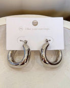 A pair of polished silver-tone hoop earrings displayed on a white branded card that reads 'i like your earrings.' The earrings have a reflective, smooth finish and are shown against a soft neutral background.