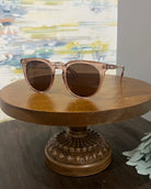 A pair of round-framed sunglasses in a taupe color, displayed on a wooden stand.