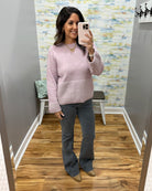 A woman takes a mirror selfie in a fitting room wearing a light pink knit sweater and dark gray flared pants.
