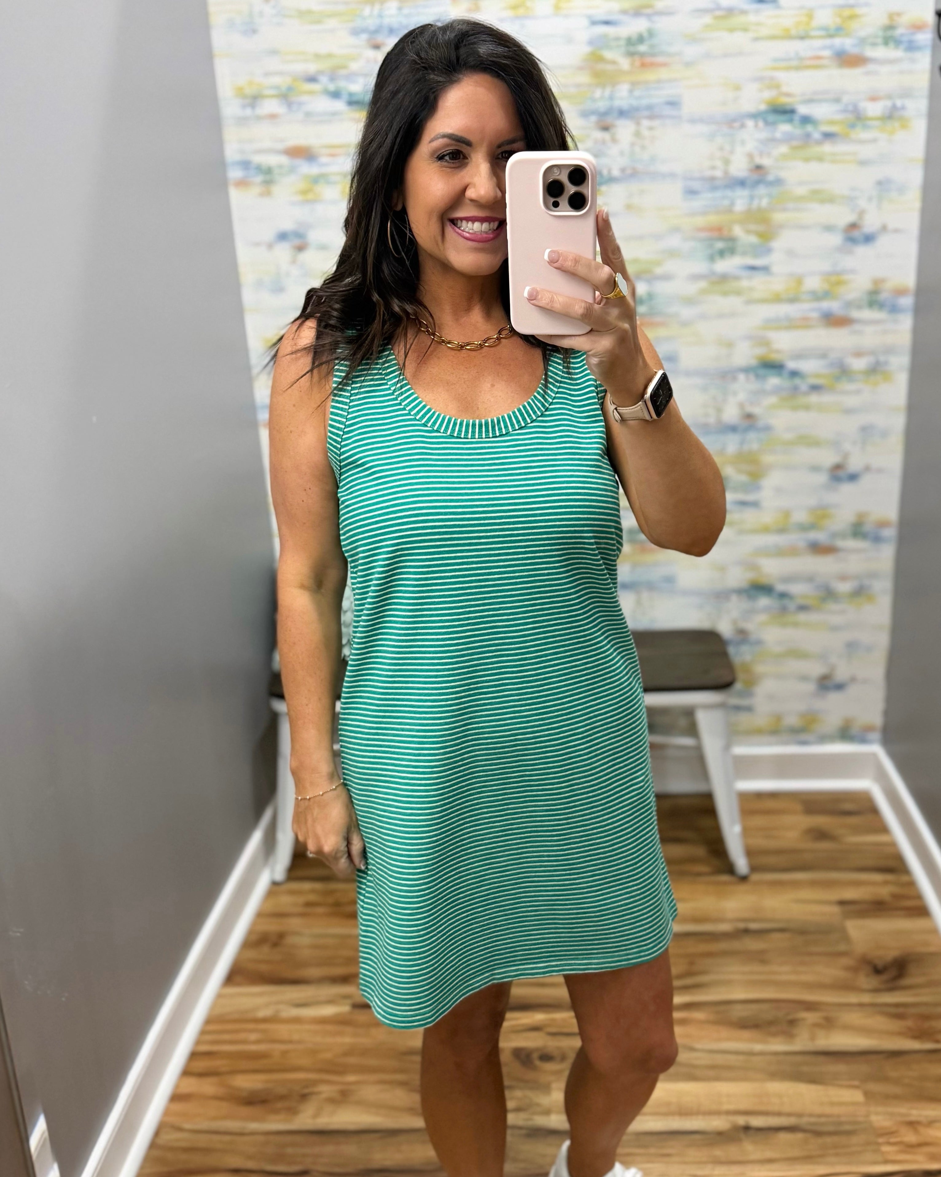 Woman taking a mirror selfie wearing a green dress in a room with a textured wall.