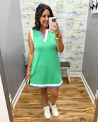 Woman taking a mirror selfie wearing a green dress with white accents in a room with a patterned wall.