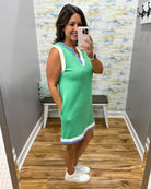 Woman taking a mirror selfie wearing a green dress with a colorful wall and wooden floor in the background.