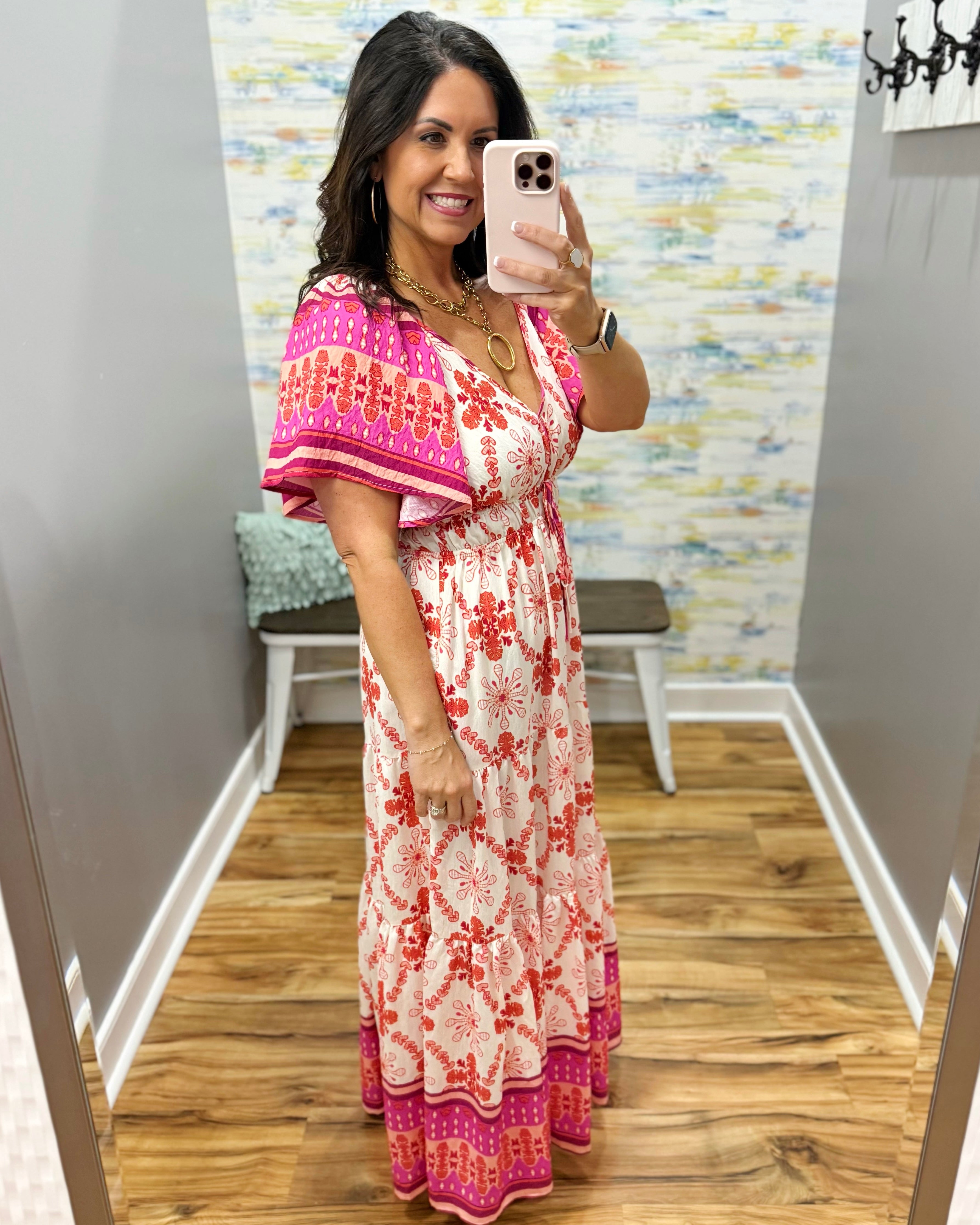 Woman taking a mirror selfie wearing a floral dress in a room with a colorful wall.