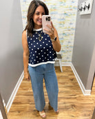Woman taking a mirror selfie wearing a navy polka dot top and blue jeans in a room with a patterned wall.