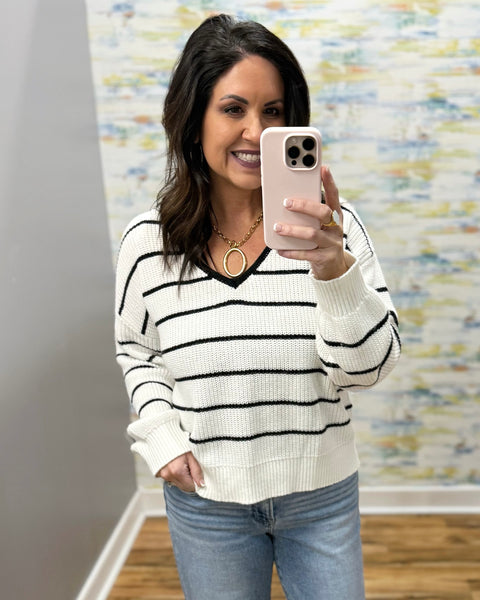 Woman taking a mirror selfie wearing a striped sweater and jeans, holding a phone.