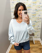 Woman taking a mirror selfie wearing a light gray sweatshirt and denim shorts.