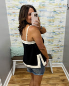 Woman taking a mirror selfie wearing a black and white tank top and denim shorts in a room with colorful wall art.