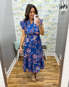 Woman taking a mirror selfie wearing a blue floral dress in a room with a textured wall.