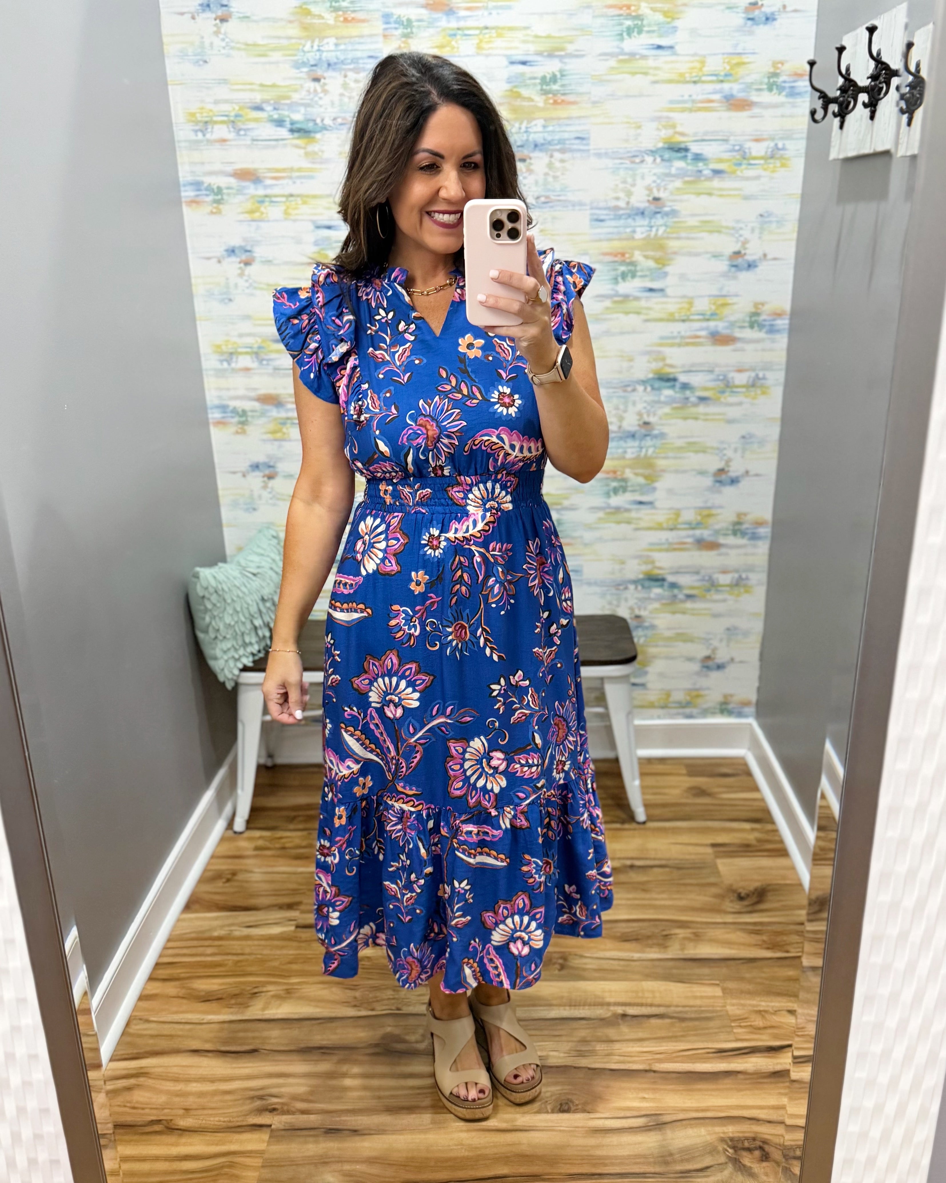 Woman taking a mirror selfie wearing a blue floral dress in a room with a textured wall.