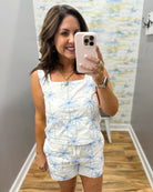 woman wearing a white top with blue palm trees embroidered on it.