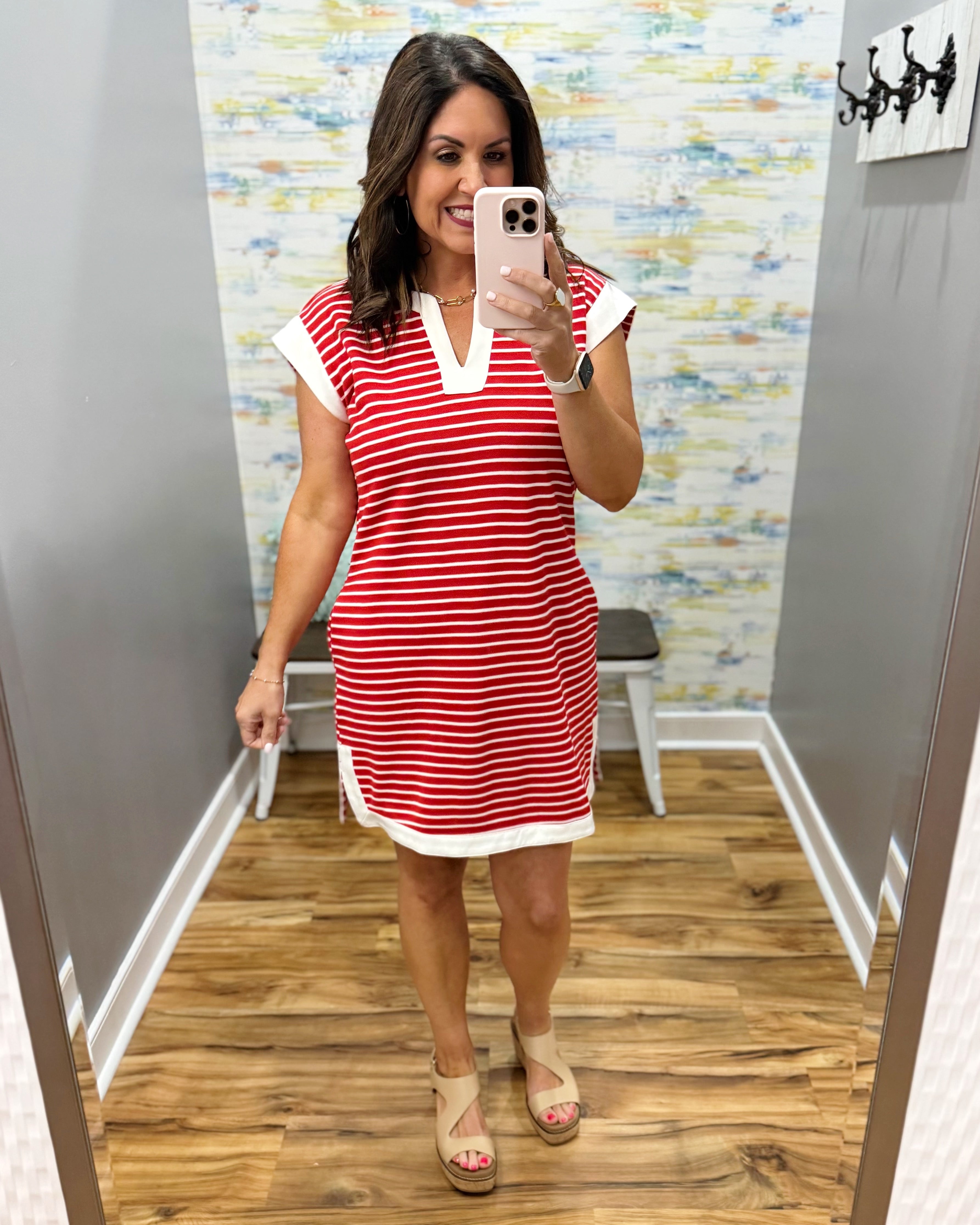 Woman taking a mirror selfie wearing a red and white striped dress in a room with a patterned wall.