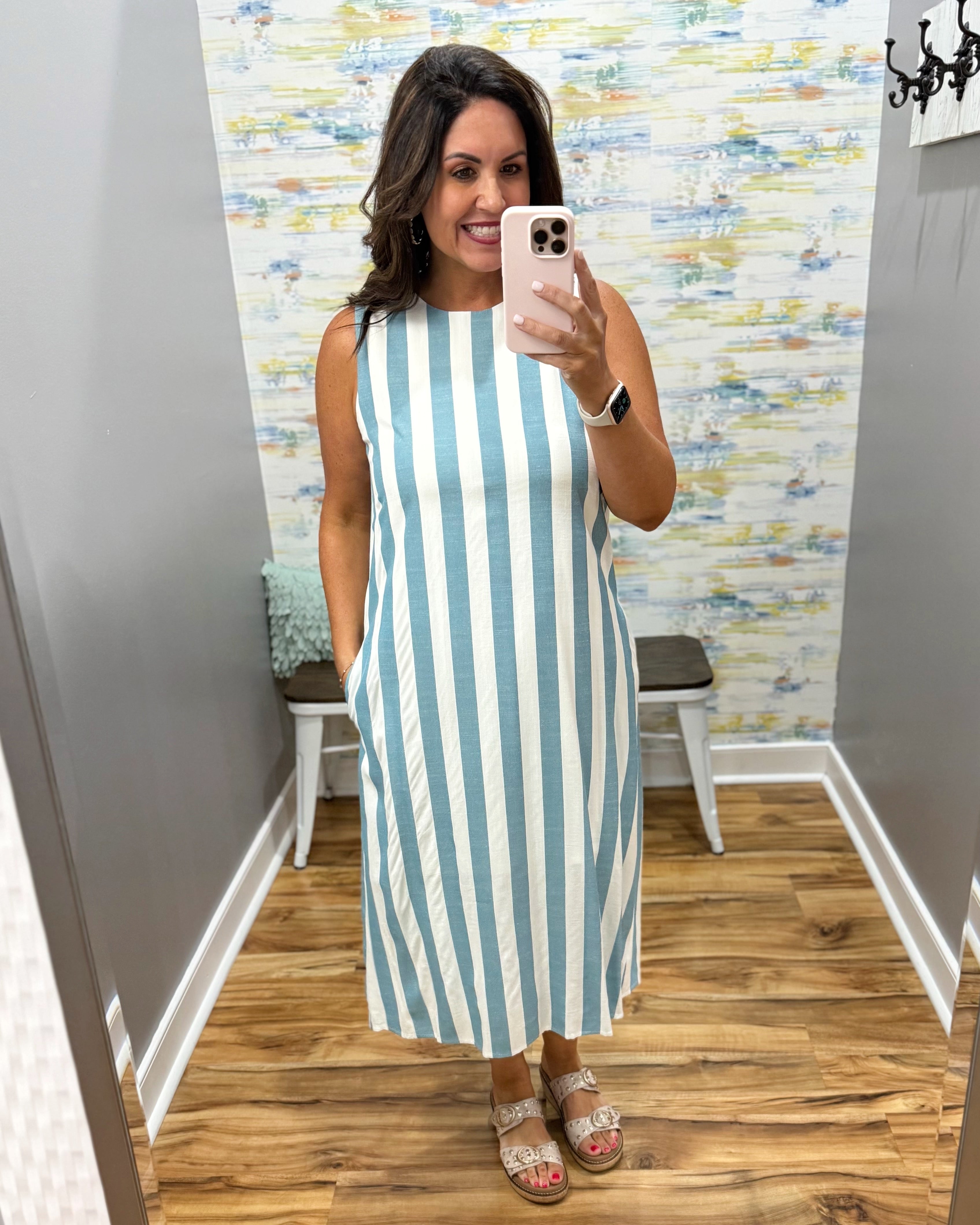Woman taking a mirror selfie wearing a blue and white striped dress in a room with patterned wallpaper.