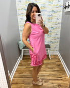 Woman taking a mirror selfie wearing a pink dress in a room with a patterned wall.