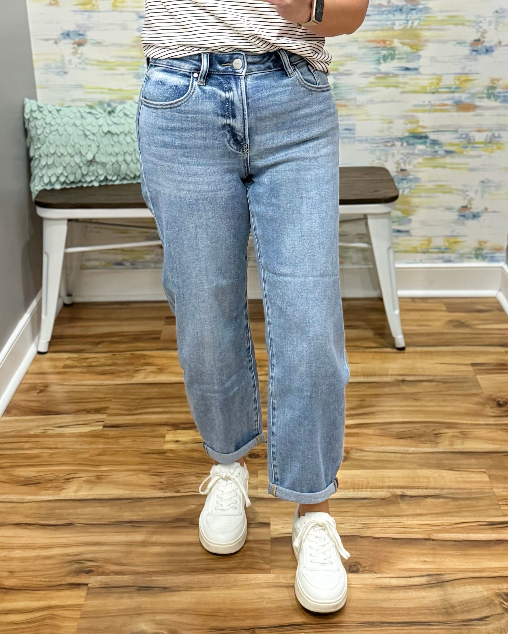 Person wearing light blue jeans and white sneakers on a wooden floor.