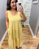 Woman wearing a yellow dress taking a mirror selfie in a room with a textured wall.
