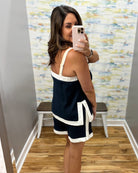 Woman taking a mirror selfie wearing a navy and white dress in a room with a colorful wall.