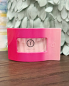 Pink container with a brand logo on a wooden surface with a decorative leafy background