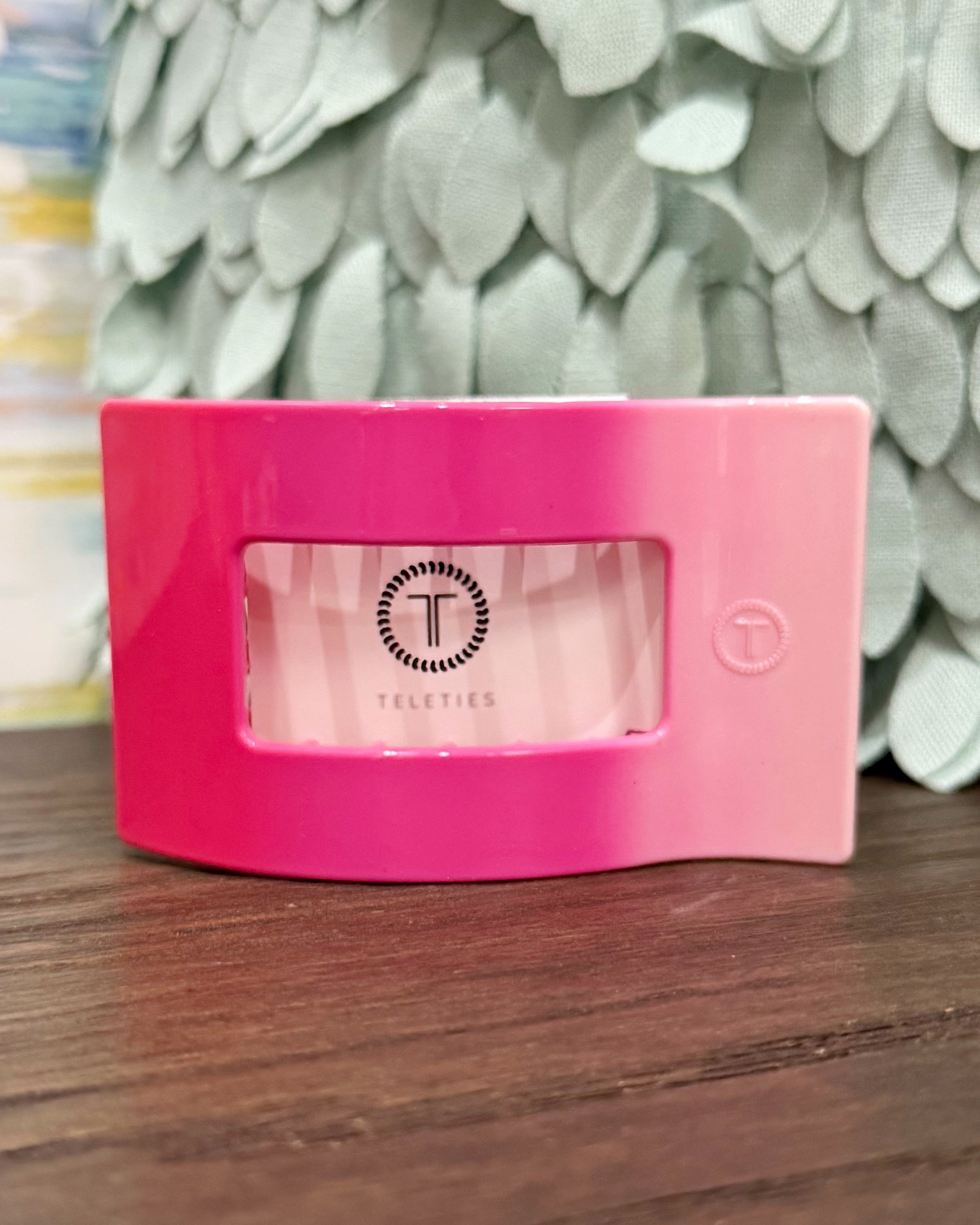 Pink container with a brand logo on a wooden surface with a decorative leafy background
