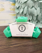 Teal hair clip with white label on a wooden surface