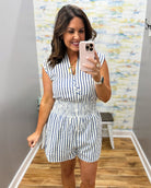 Woman taking a mirror selfie wearing a striped romper in a room with a colorful wall.