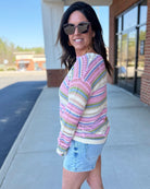 Woman wearing a colorful striped sweater and denim shorts outdoors.