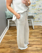 Person wearing a light gray outfit with wide-leg pants in a room with wooden flooring and a colorful wall.