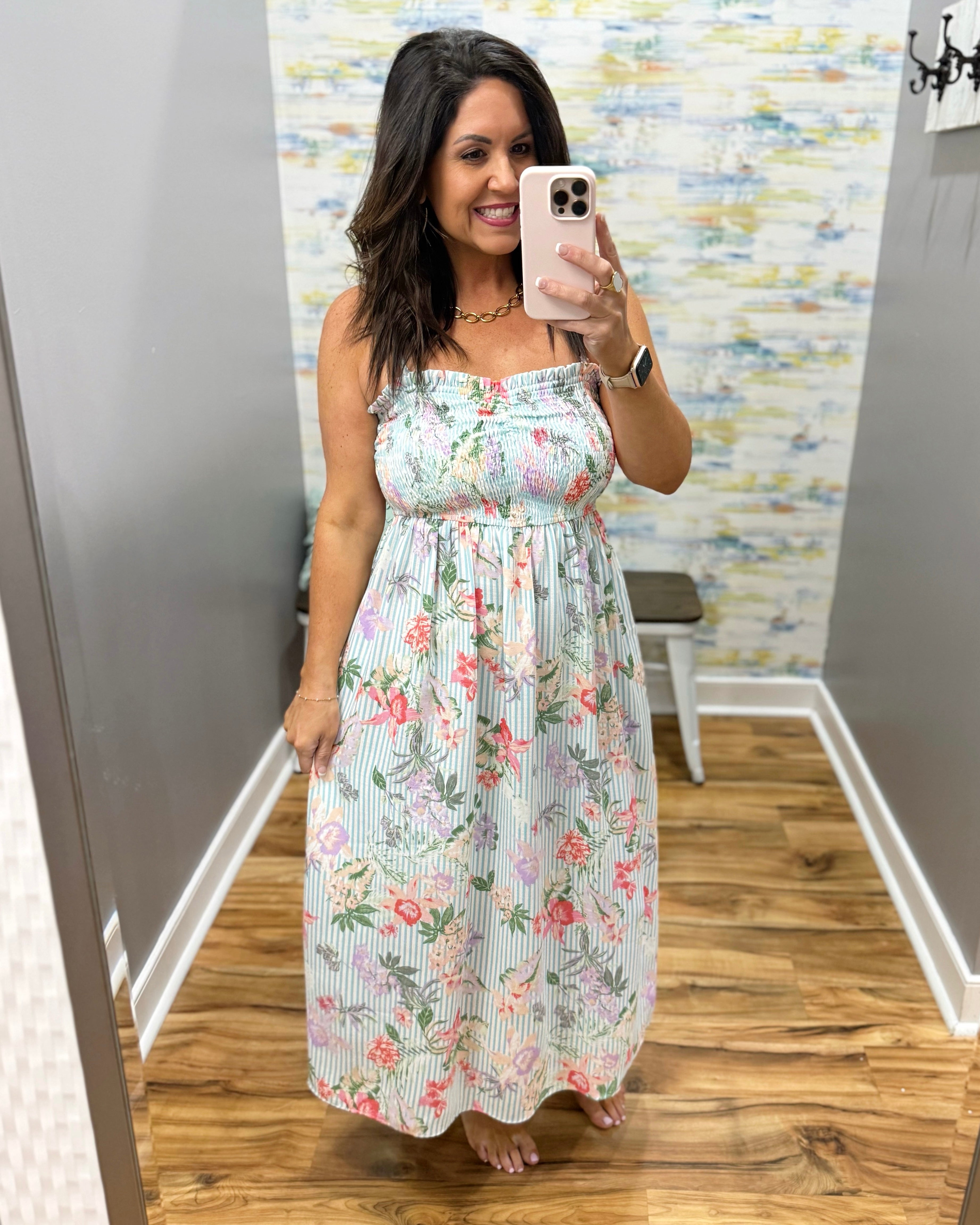 Woman taking a mirror selfie wearing a floral dress in a room with a patterned wall.