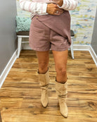 A person wearing a chestnut color wrap-style mini skirt with a single button closure, paired with a pink and white striped long-sleeve top and Corkys City Slicker boots in Sand Faux Suede.
