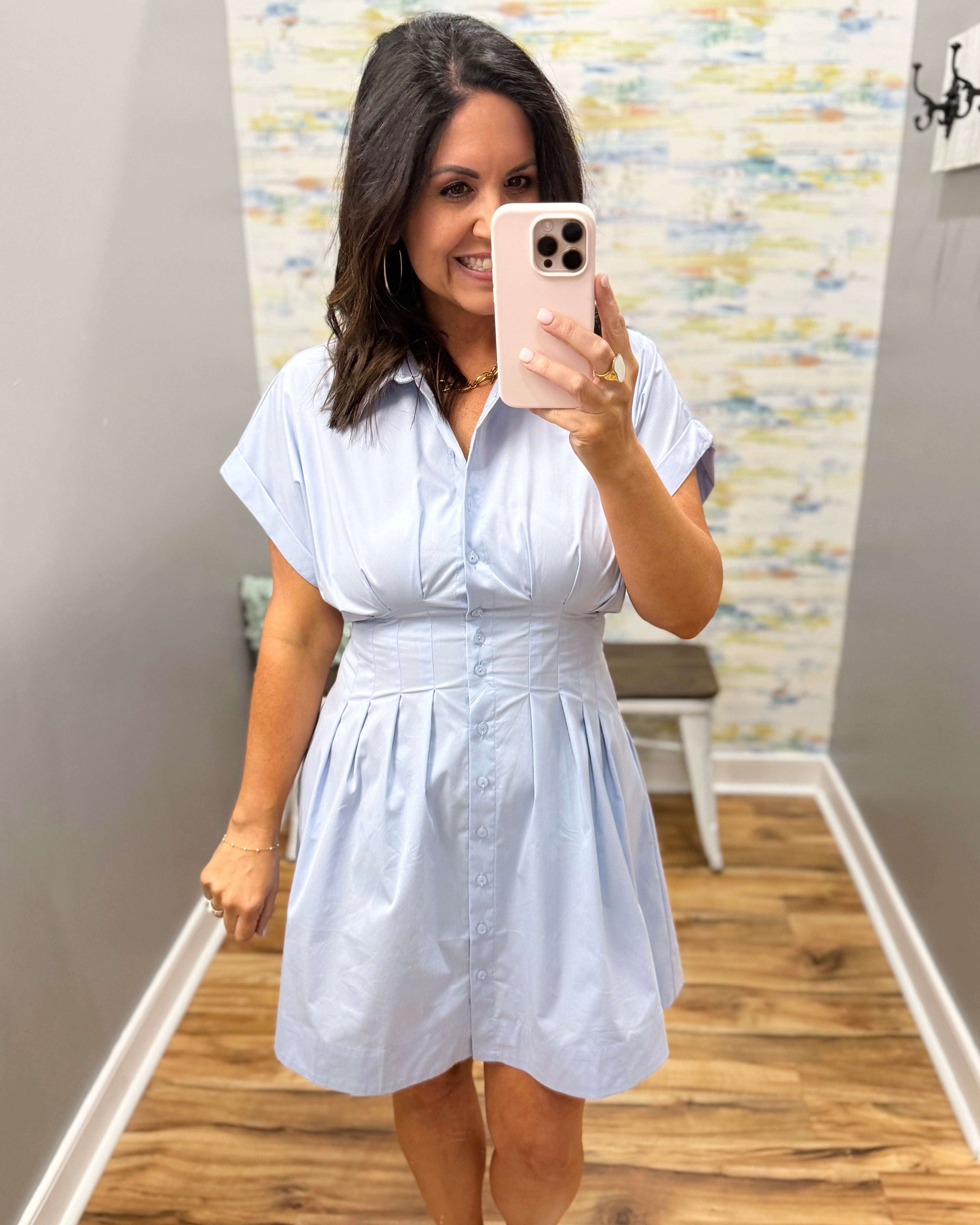 Woman taking a mirror selfie wearing a light blue dress in a room with a patterned wall.