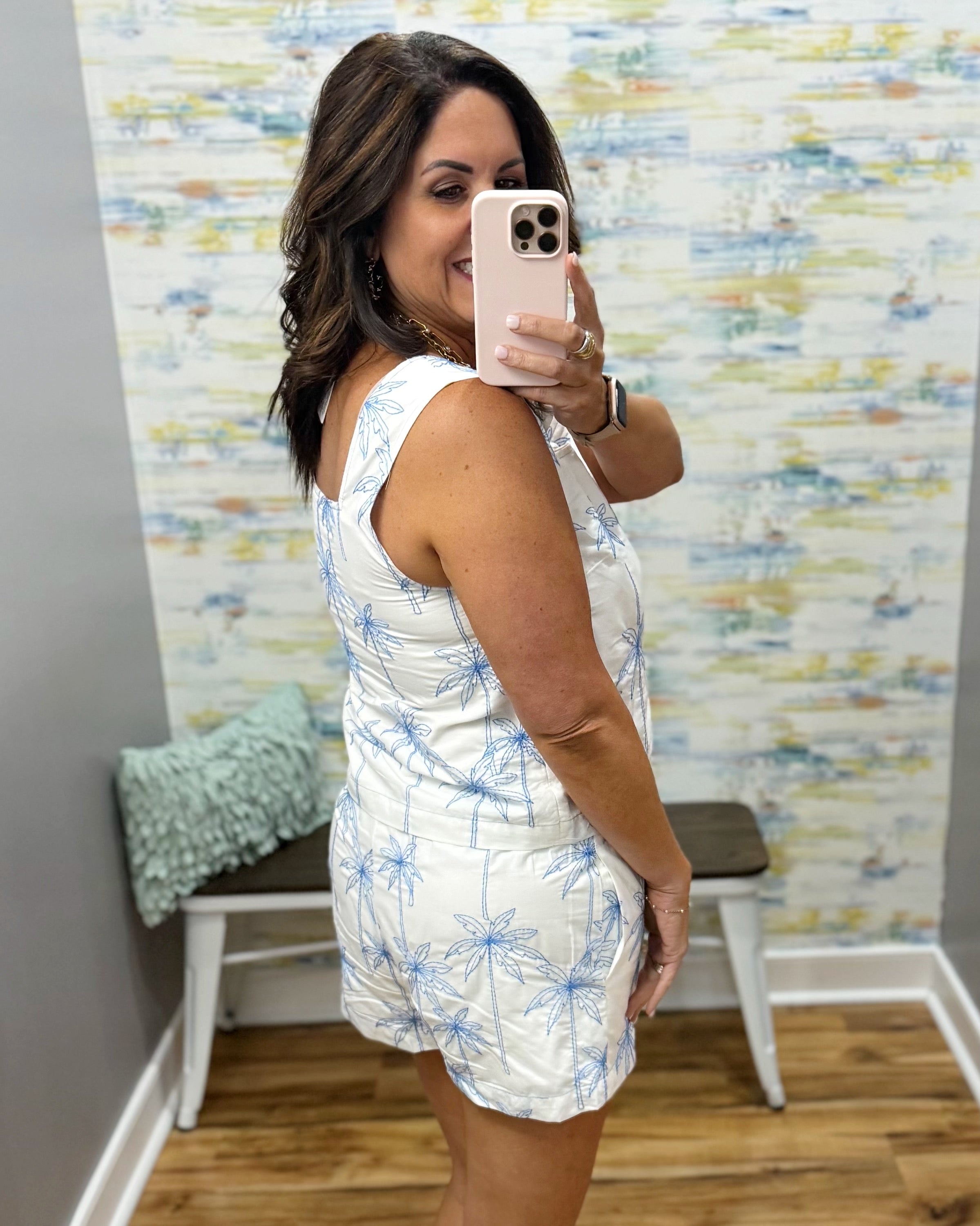 woman wearing a white top and shorts with blue palm trees embroidered on them.
