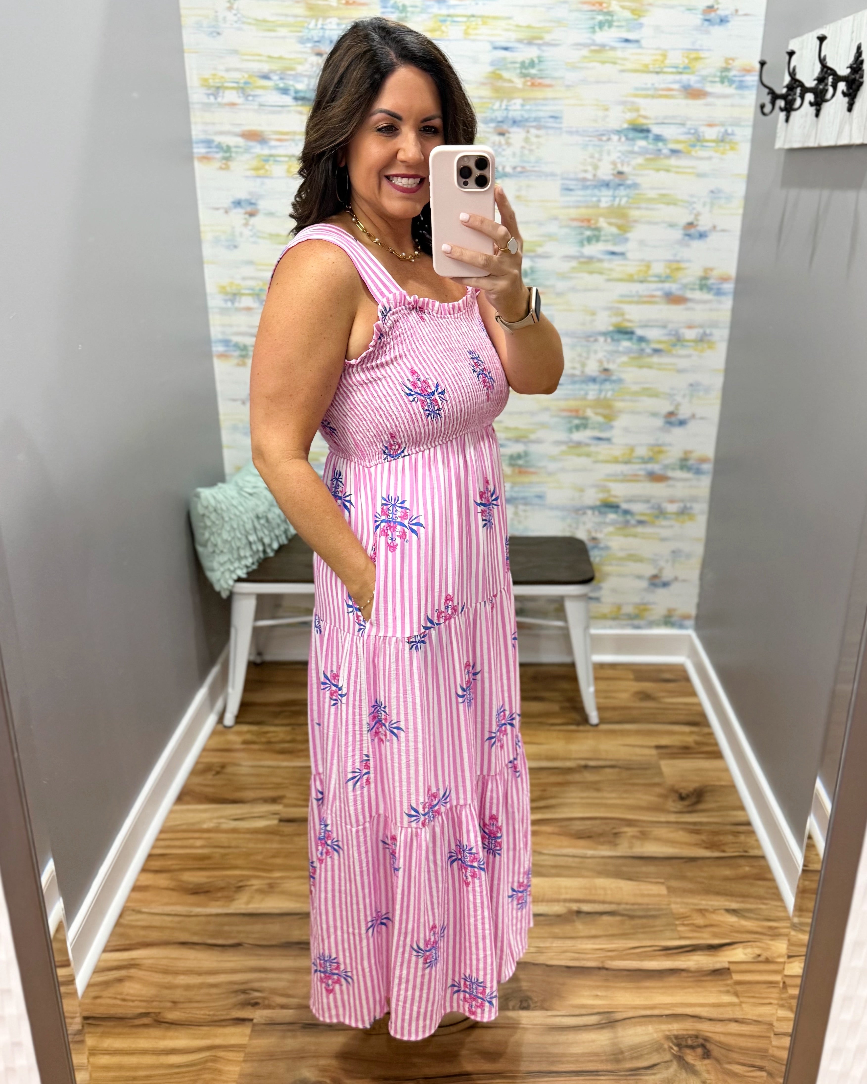 Woman taking a mirror selfie wearing a pink dress with floral patterns in a room with a colorful wall.